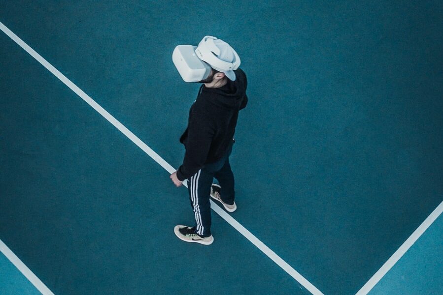 man in track suit wearing VR headset standing on tennis court